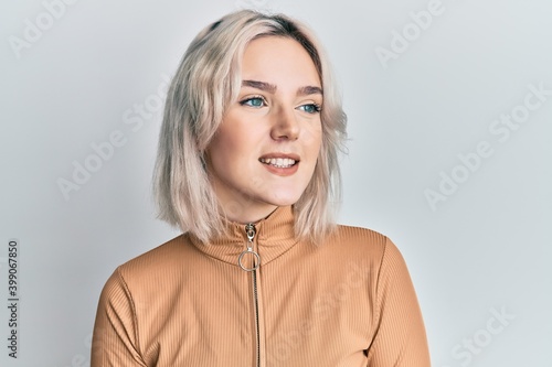 Young blonde girl wearing casual clothes looking away to side with smile on face, natural expression. laughing confident.