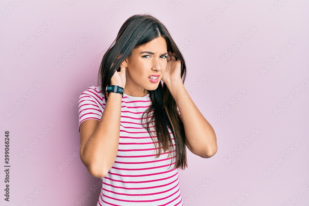 Young brunette woman wearing casual clothes over pink background trying to hear both hands on ear gesture, curious for gossip. hearing problem, deaf Young brunette woman wearing casual clothes over pink background trying to hear both hands on ear gesture, curious for gossip. hearing problem, deaf