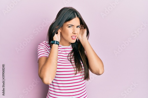 Young brunette woman wearing casual clothes over pink background trying to hear both hands on ear gesture, curious for gossip. hearing problem, deaf