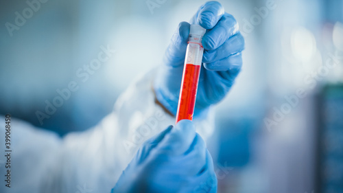 Medical Research Scientist Wearing Coverall, Surgical Gloves Holds Test Tube with Blood Sample and Label Reading Coronavirus. Microbiology Laboratory Drug and Vaccine Development