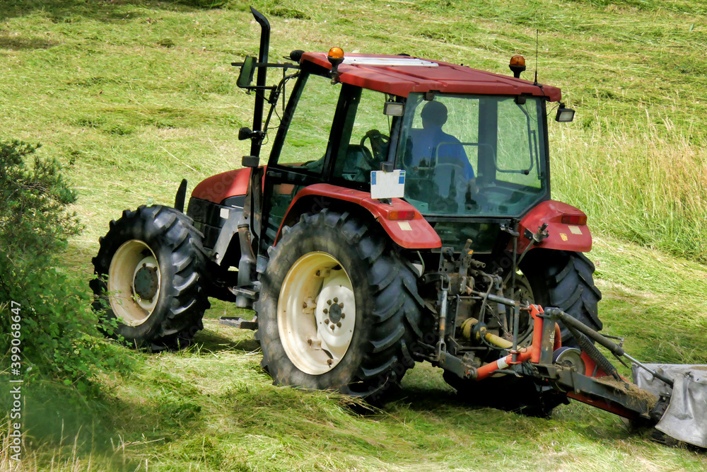 Tractor cutting grass in a field prior to drying and baling Tractor cutting grass in a field prior to drying and baling