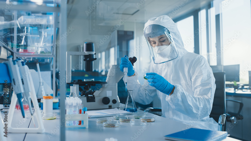 Beautiful Female Medical Scientist Wearing Coverall and Face Mask Using Micro Pipette while Working with Test Tubes. Vaccine, Drugs Research and Development Laboratory with Modern Equipment Beautiful Female Medical Scientist Wearing Coverall and Face Mask Using Micro Pipette while Working with Test Tubes. Vaccine, Drugs Research and Development Laboratory with Modern Equipment