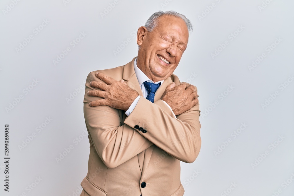 Senior caucasian man wearing business suit hugging oneself happy and positive, smiling confident. self love and self care