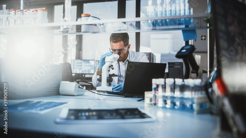 In Bright Medical Science Laboratory  Brilliant Microbiologist Looks Under Microscope Does Analysis of Test Sample. Team of Research Scientists working with High-Tech Equipment and Glassware