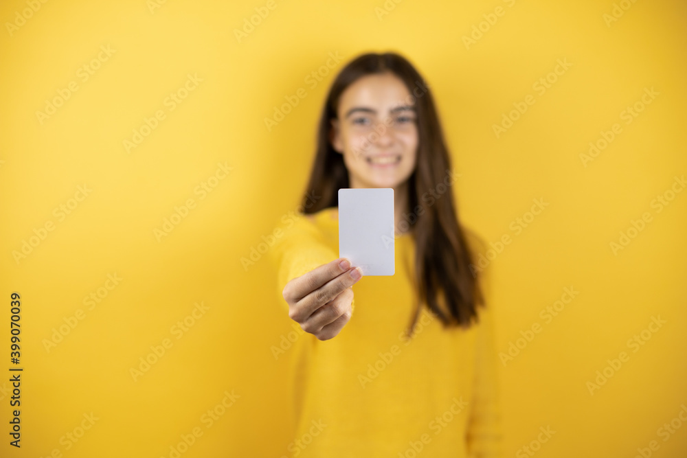Pretty girl wearing a yellow sweater standing over isolated yellow background holding white card Pretty girl wearing a yellow sweater standing over isolated yellow background holding white card