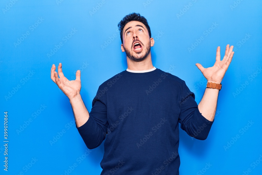 Naklejka premium Young hispanic man wearing casual clothes crazy and mad shouting and yelling with aggressive expression and arms raised. frustration concept.
