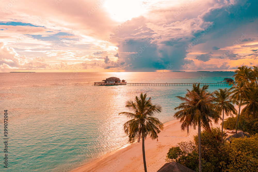 Aerial sunrise sunset beach bay view, colorful sky and clouds, wooden jetty over water bungalow. Meditation relaxation tropical drone view, sea ocean water. Aerial nature skyscape seascape background