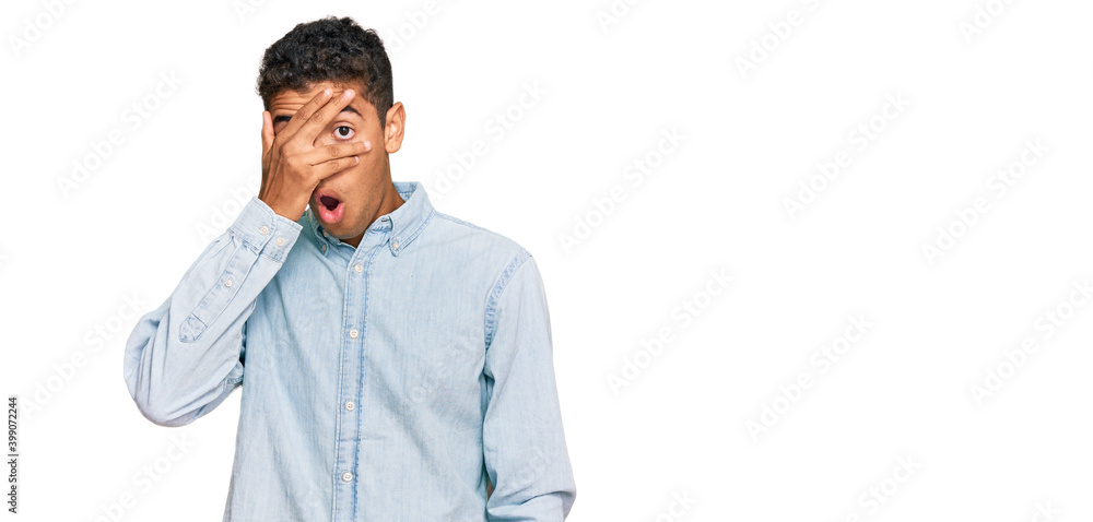 Young handsome african american man wearing casual clothes peeking in shock covering face and eyes with hand, looking through fingers with embarrassed expression. Young handsome african american man wearing casual clothes peeking in shock covering face and eyes with hand, looking through fingers with embarrassed expression.