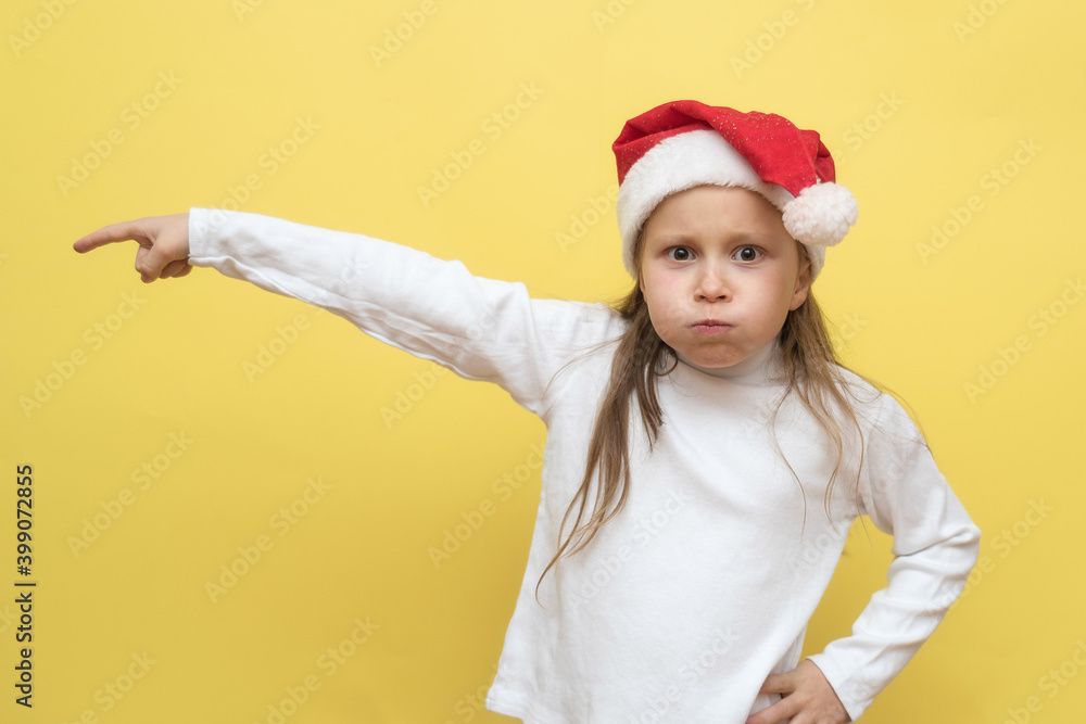 Cute little girl in a Christmas hat. The girl shows emotions on a yellow background. New year concept. Cute little girl in a Christmas hat. The girl shows emotions on a yellow background. New year concept.