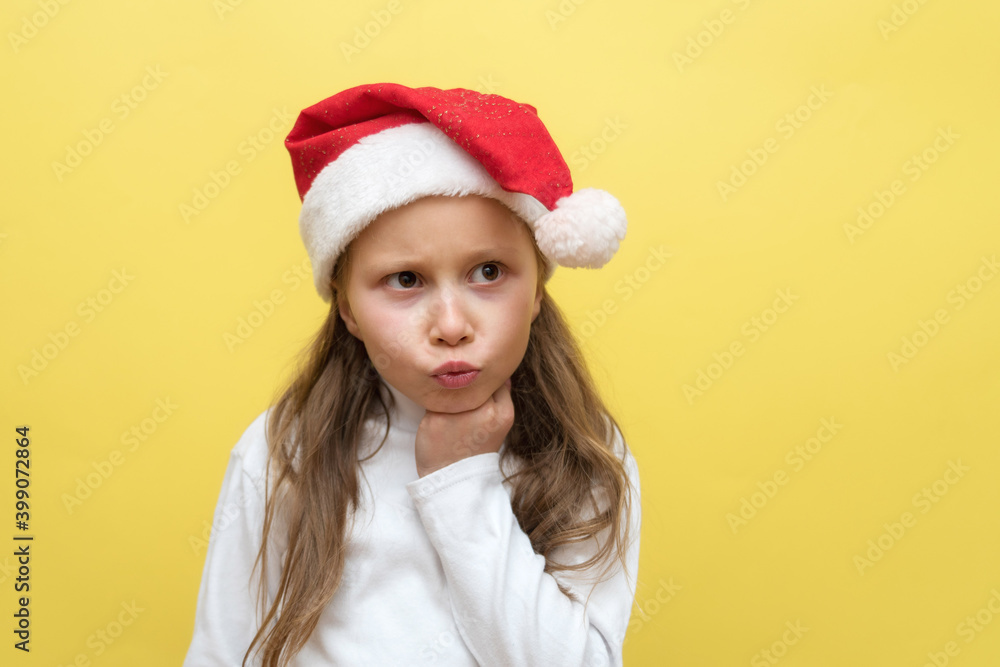 Cute little girl in a Christmas hat. The girl shows emotions on a yellow background. New year concept. Cute little girl in a Christmas hat. The girl shows emotions on a yellow background. New year concept.