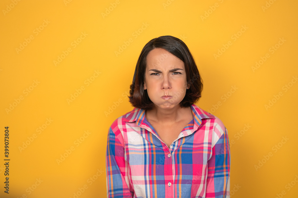 Making funny faces pretty looking girl looking to camera. Woman in a plaid shirt on yellow background. Human emotions, facial expression concept. Making funny faces pretty looking girl looking to camera. Woman in a plaid shirt on yellow background. Human emotions, facial expression concept.