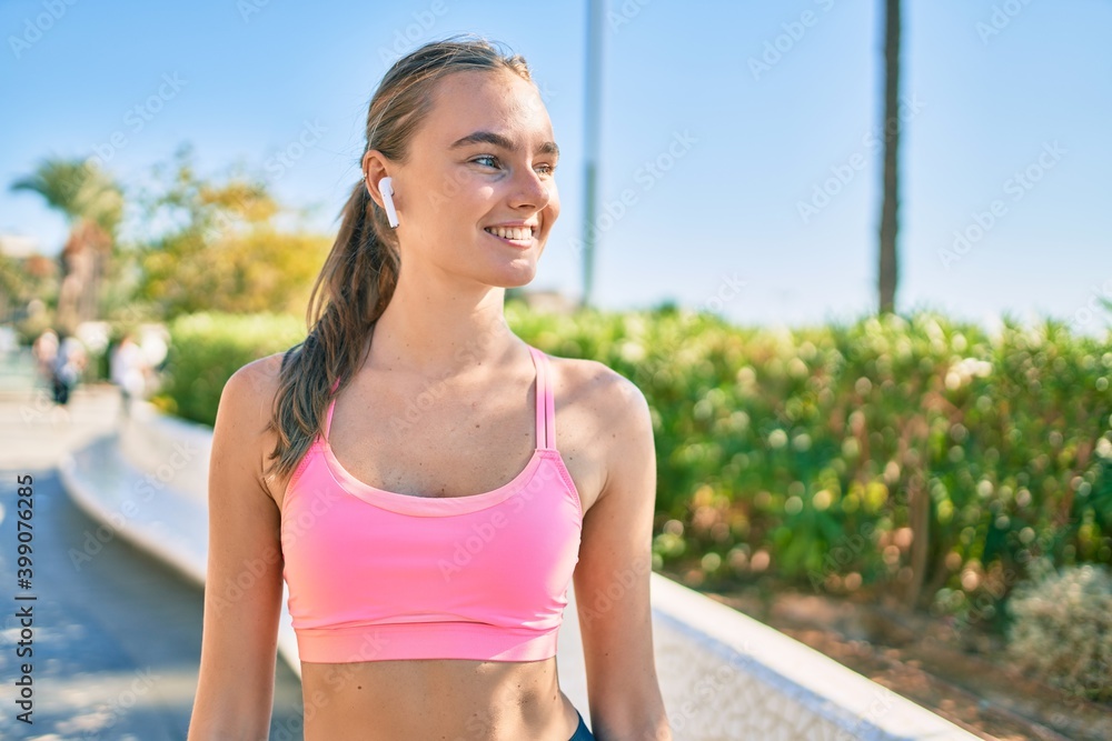 Young blonde sportswoman using earphones doing exercise at the city Young blonde sportswoman using earphones doing exercise at the city