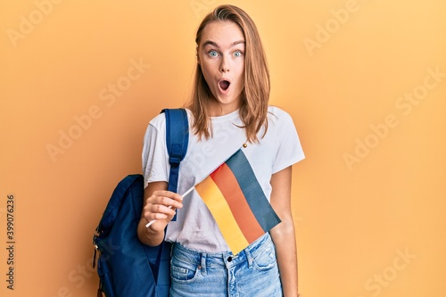 Beautiful blonde woman exchange student holding germany flag scared and amazed with open mouth for surprise, disbelief face