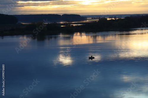 Early morning on the river with blue water and Golden sky.The rising sun highlights the clouds and water expanses of the lake with a fisherman in a boat in the center.Colorful image of nature at dawn