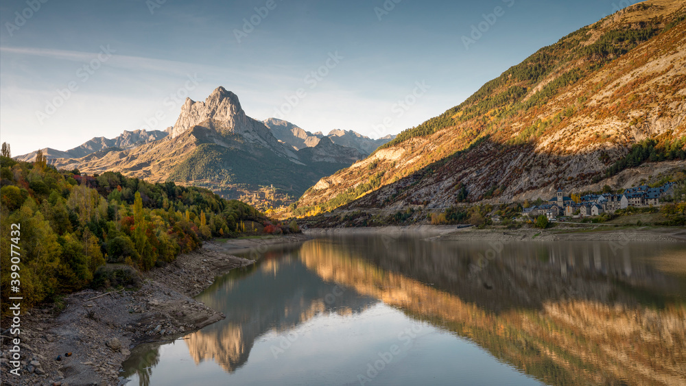 Mountain with water refllection in a lake with autumn tree forest and a small town in Aragon, Heusca, Spain