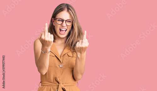 Obraz na plátně Young beautiful blonde woman wearing casual clothes and glasses showing middle finger doing fuck you bad expression, provocation and rude attitude