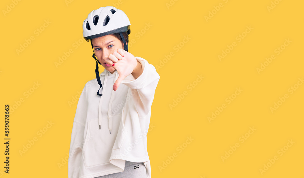 Beautiful brunette young woman wearing bike helmet and sporty clothes looking unhappy and angry showing rejection and negative with thumbs down gesture. bad expression. Beautiful brunette young woman wearing bike helmet and sporty clothes looking unhappy and angry showing rejection and negative with thumbs down gesture. bad expression.