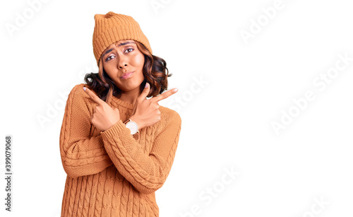 Young beautiful mixed race woman wearing wool sweater and winter hat pointing to both sides with fingers, different direction disagree photo