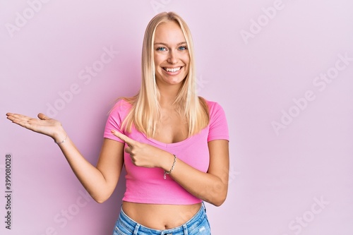 Young blonde girl wearing casual clothes amazed and smiling to the camera while presenting with hand and pointing with finger. © Krakenimages.com
