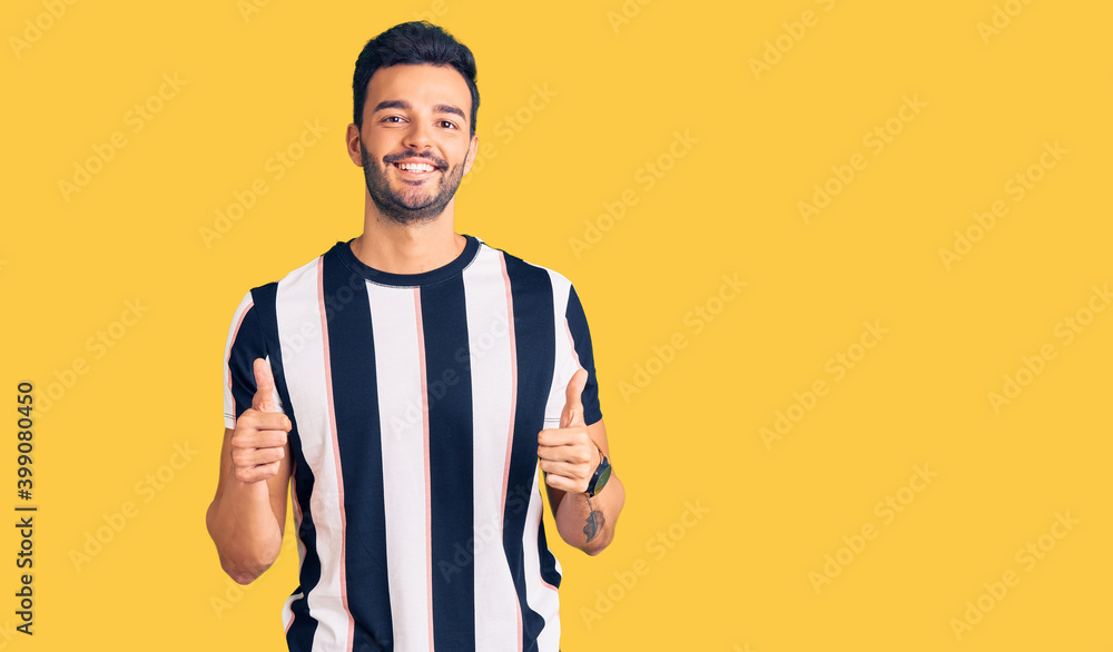 Young handsome hispanic man wearing striped tshirt success sign doing positive gesture with hand, thumbs up smiling and happy. cheerful expression and winner gesture. Young handsome hispanic man wearing striped tshirt success sign doing positive gesture with hand, thumbs up smiling and happy. cheerful expression and winner gesture.