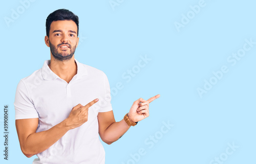 Young handsome hispanic man wearing casual clothes pointing aside worried and nervous with both hands, concerned and surprised expression