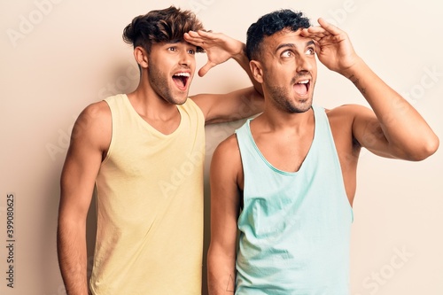 Young gay couple wearing casual clothes very happy and smiling looking far away with hand over head. searching concept. © Krakenimages.com