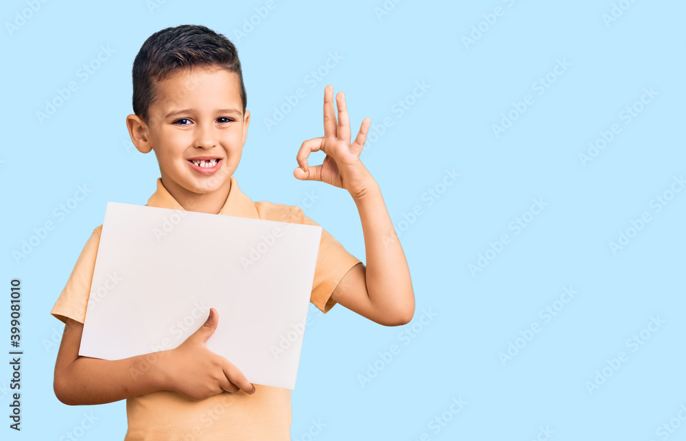 Little cute boy kid holding cardboard banner with blank space doing ok sign with fingers, smiling friendly gesturing excellent symbol Little cute boy kid holding cardboard banner with blank space doing ok sign with fingers, smiling friendly gesturing excellent symbol