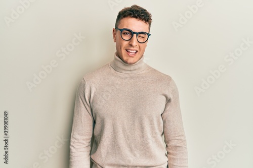 Hispanic young man wearing casual turtleneck sweater winking looking at the camera with sexy expression, cheerful and happy face. © Krakenimages.com