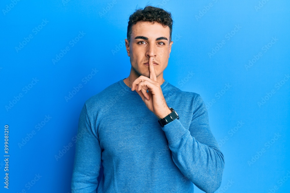 Hispanic young man wearing casual winter sweater asking to be quiet with finger on lips. silence and secret concept.