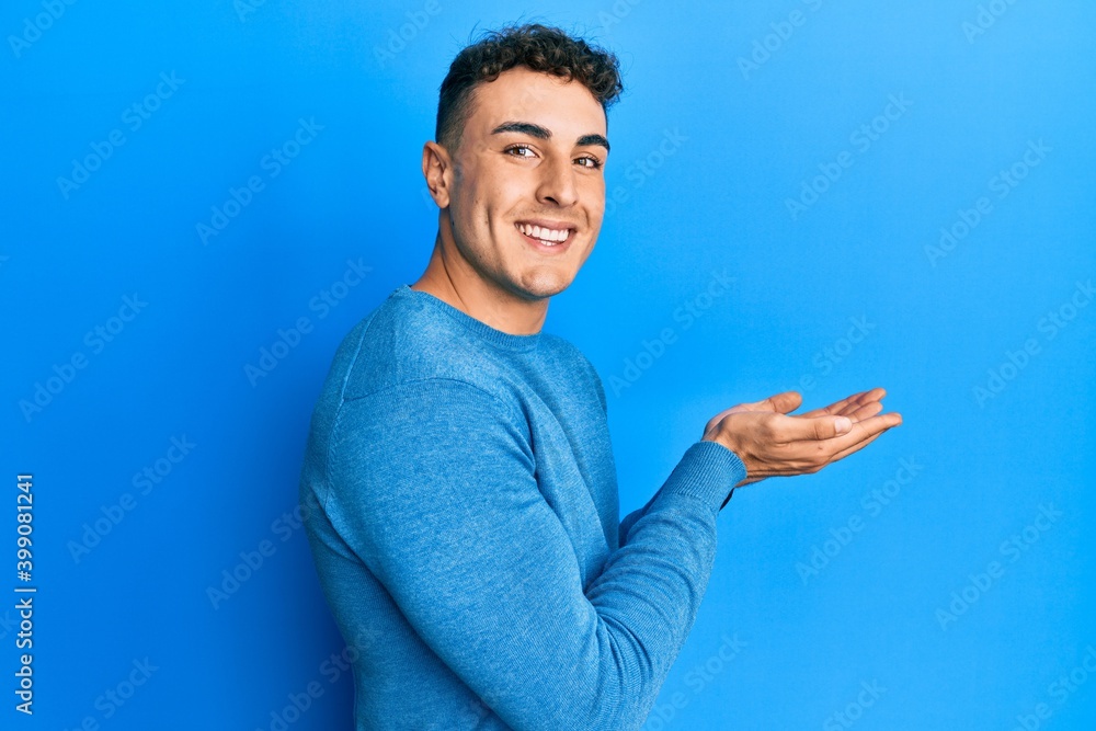Hispanic young man wearing casual winter sweater pointing aside with hands open palms showing copy space, presenting advertisement smiling excited happy Hispanic young man wearing casual winter sweater pointing aside with hands open palms showing copy space, presenting advertisement smiling excited happy