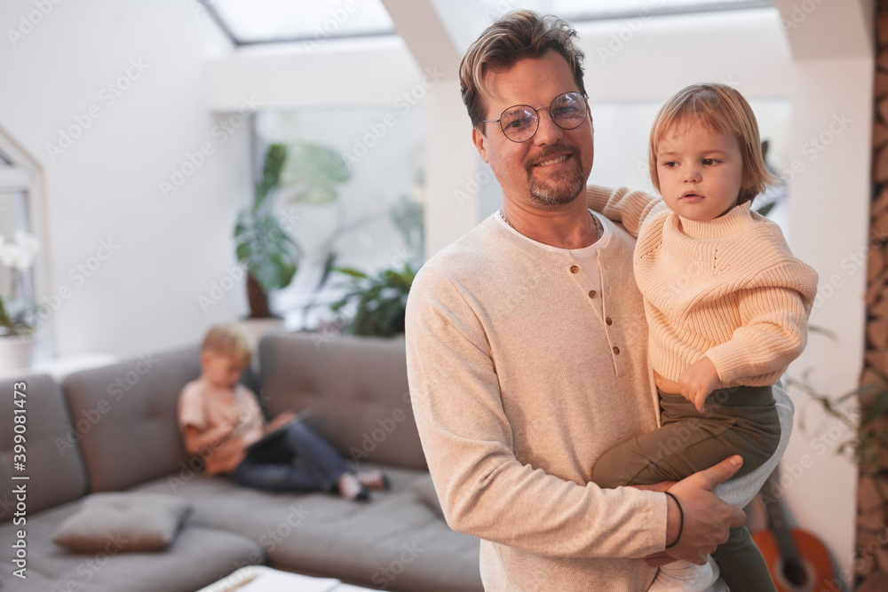 Waist up portrait of happy mature father holding cute little girl and looking at camera while standing in modern home interior, copy space Waist up portrait of happy mature father holding cute little girl and looking at camera while standing in modern home interior, copy space