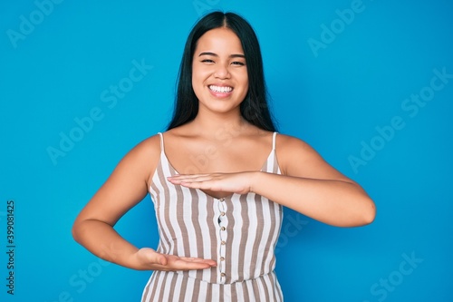 Young beautiful asian girl wearing casual clothes gesturing with hands showing big and large size sign, measure symbol. smiling looking at the camera. measuring concept.