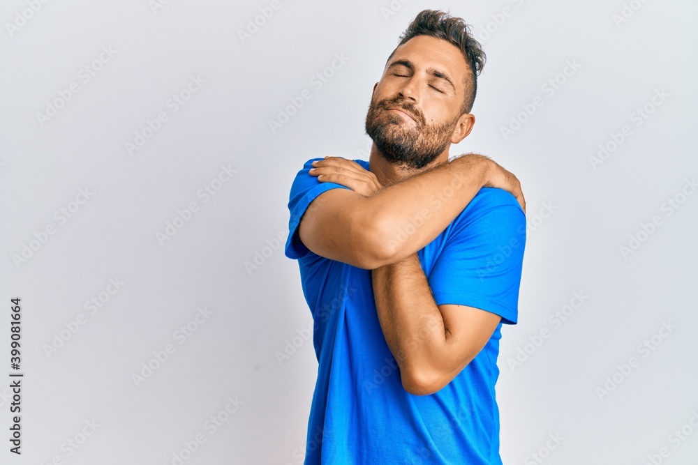 Handsome man with beard wearing casual clothes hugging oneself happy and positive, smiling confident. self love and self care Handsome man with beard wearing casual clothes hugging oneself happy and positive, smiling confident. self love and self care