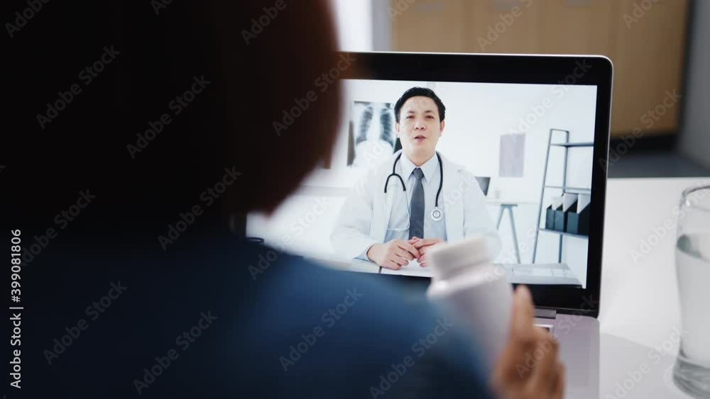 Young Asia lady using computer laptop talk about a disease in video conference call with senior doctor online consultation in living room at home. Social distancing, quarantine for coronavirus concept Young Asia lady using computer laptop talk about a disease in video conference call with senior doctor online consultation in living room at home. Social distancing, quarantine for coronavirus concept
