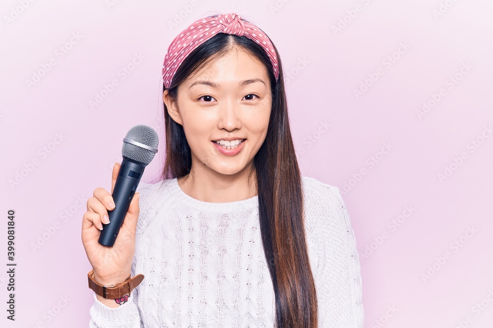 Young beautiful chinese woman singing song using microphone looking positive and happy standing and smiling with a confident smile showing teeth Young beautiful chinese woman singing song using microphone looking positive and happy standing and smiling with a confident smile showing teeth