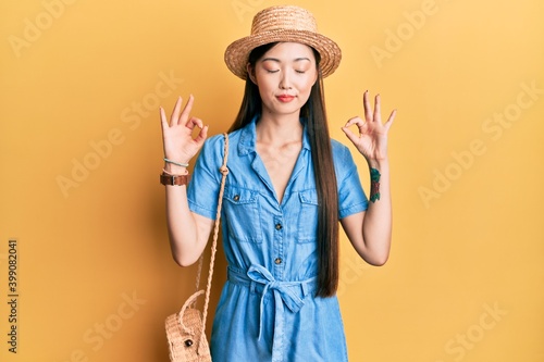Young chinese woman wearing summer hat relax and smiling with eyes closed doing meditation gesture with fingers. yoga concept.