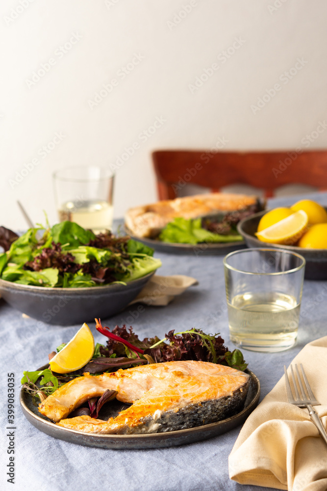Fried salmon steak with salad in a plate , white wine in a glass, delicious hearty dinner or lunch Fried salmon steak with salad in a plate , white wine in a glass, delicious hearty dinner or lunch