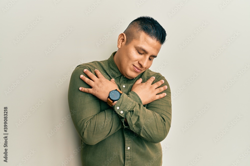 Young latin man wearing casual clothes hugging oneself happy and positive, smiling confident. self love and self care Young latin man wearing casual clothes hugging oneself happy and positive, smiling confident. self love and self care