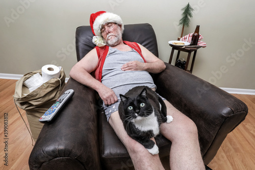 Quarantine Santa Claus sleeping in an recliner with face mask and sack full of toilet paper with his cat on his lap
