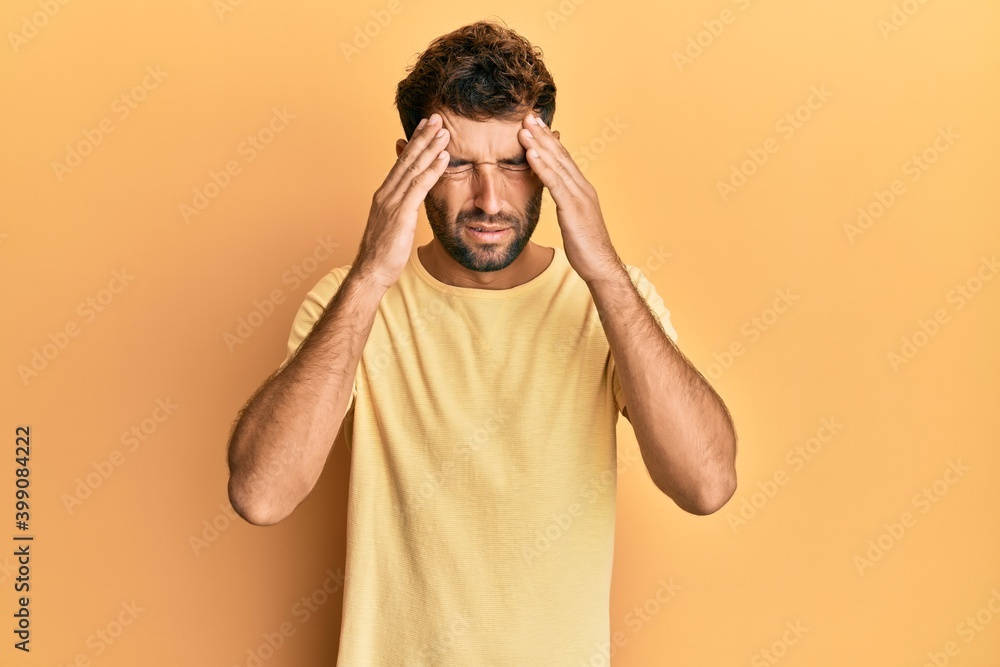 Handsome man with beard wearing casual yellow tshirt over yellow background with hand on head for pain in head because stress. suffering migraine. Handsome man with beard wearing casual yellow tshirt over yellow background with hand on head for pain in head because stress. suffering migraine.