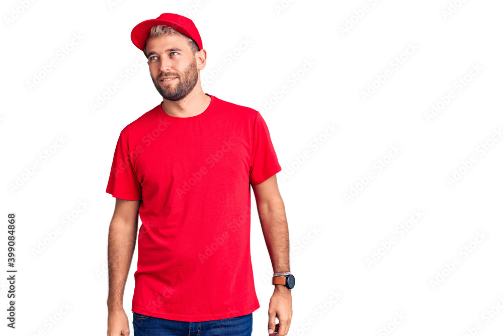 Young handsome blond man wearing t-shirt and cap looking away to side with smile on face, natural expression. laughing confident.