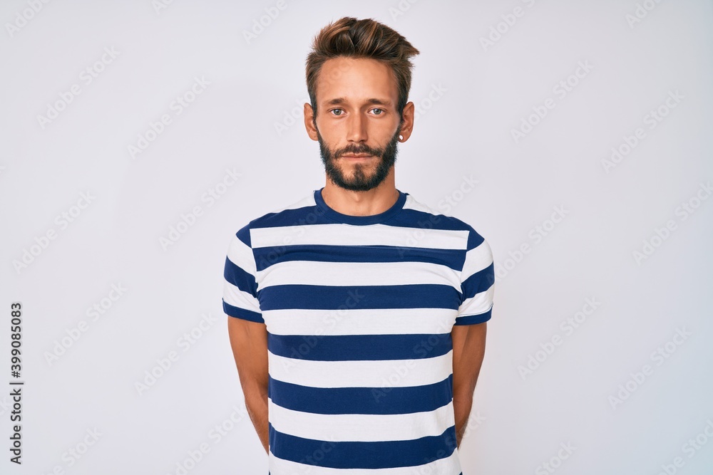 Handsome caucasian man with beard wearing casual striped t-shirt with serious expression on face. simple and natural looking at the camera. Handsome caucasian man with beard wearing casual striped t-shirt with serious expression on face. simple and natural looking at the camera.