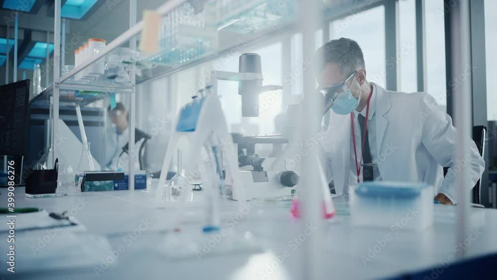 Medical Development Laboratory: Scientist Wearing Face Mask Looking Under Microscope, Enters Data into Digital Tablet. Specialists Working on Medicine, Biotechnology Research in Advanced Pharma Lab Medical Development Laboratory: Scientist Wearing Face Mask Looking Under Microscope, Enters Data into Digital Tablet. Specialists Working on Medicine, Biotechnology Research in Advanced Pharma Lab