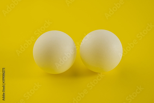Two white tennis balls lie on a yellow trending background.