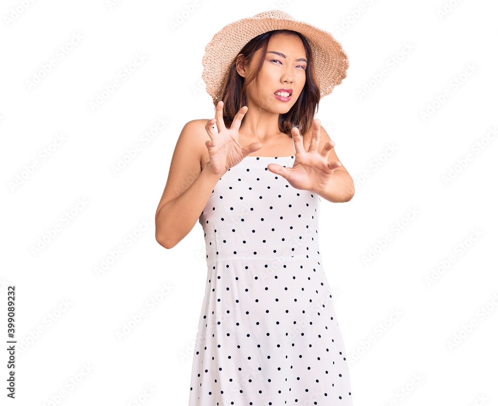 Young beautiful chinese girl wearing summer hat disgusted expression, displeased and fearful doing disgust face because aversion reaction. with hands raised Young beautiful chinese girl wearing summer hat disgusted expression, displeased and fearful doing disgust face because aversion reaction. with hands raised