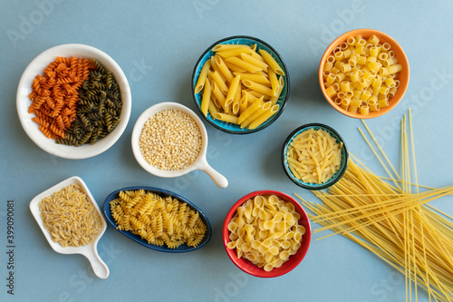 pasta in ceramic bowl. penne, spaghetti, farfalle tonde, butterfly, auger, couscous, colorful pasta, barley noodle, kesme, egg, erişte, ditalini type pasta on blue background. orange white red