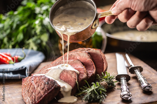 Fotografie Rump steak cut to slices on a chopping board next to a knife and rosemary, with