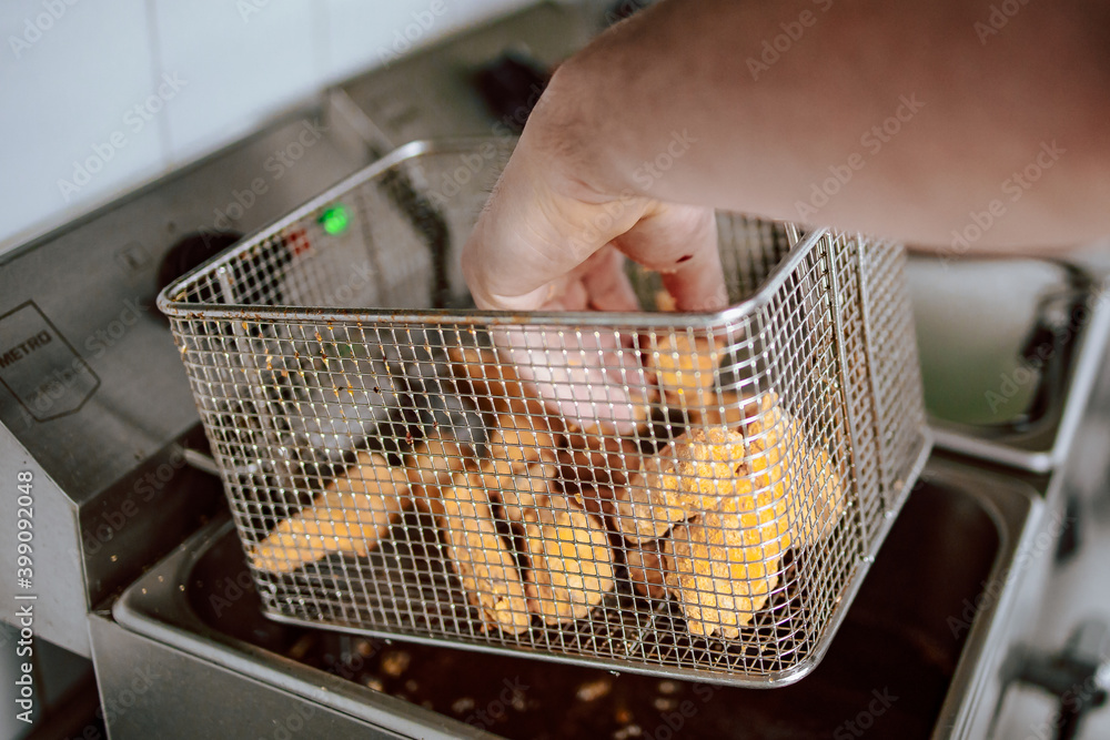Chef putting frozen chicken nuggets in deep fryer. Restaurant meal
