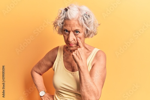 Senior grey-haired woman wearing casual clothes pointing to the eye watching you gesture, suspicious expression