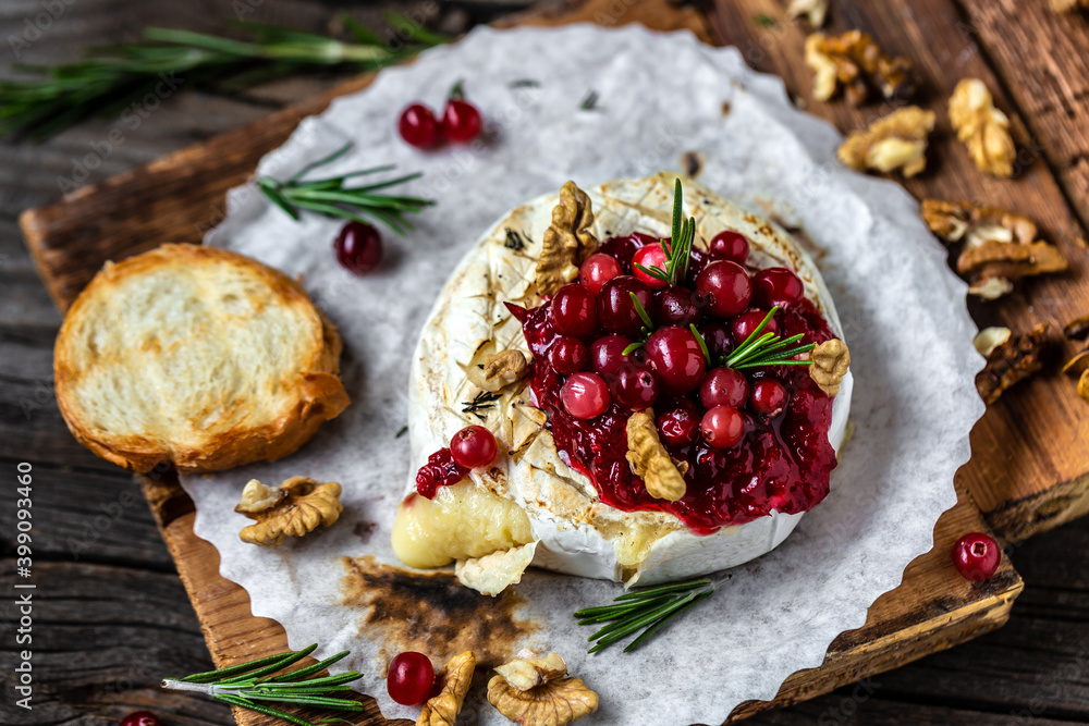 Baked camembert with cranberry sauce, baguette bread and rosemary on rustic wooden table
